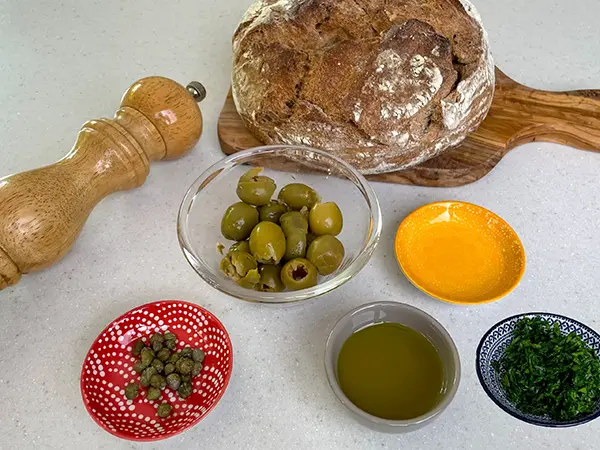 olivada ingredients including pitted olives, olive oil, lemon, blackpepper and parsley