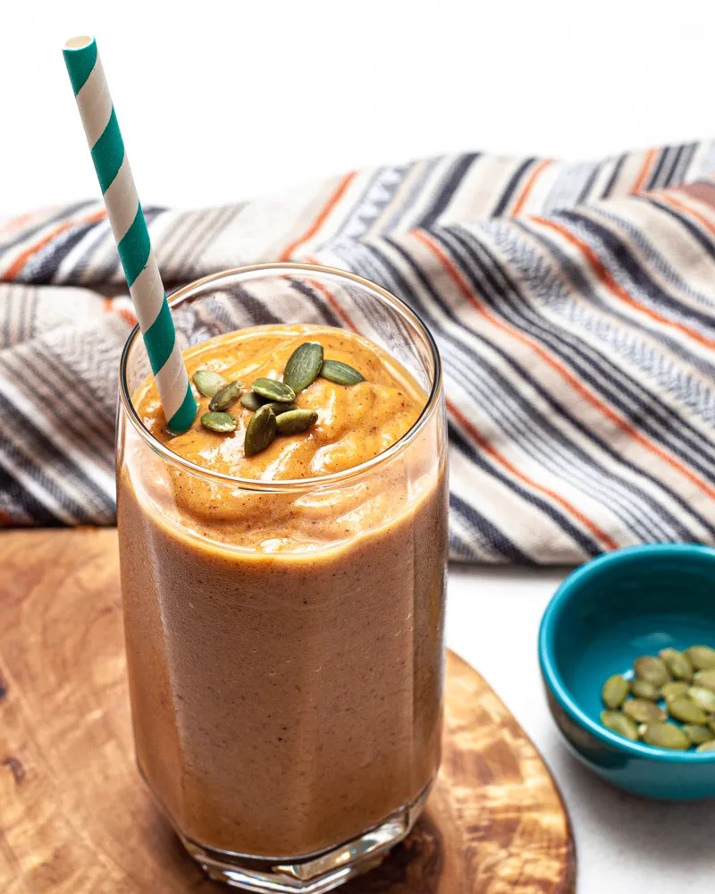 glass of spiced pumpkin smoothie with straw and pumpkin seeds