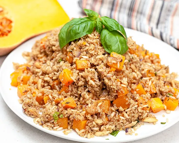 Serving dish of butternut squash made with brown rice and quinoa decorated with basil leaves